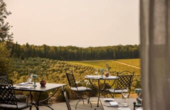 Outdoor dining tables with iron chairs set with glassware and napkins overlooking hills and vineyards at Podere San Filippo