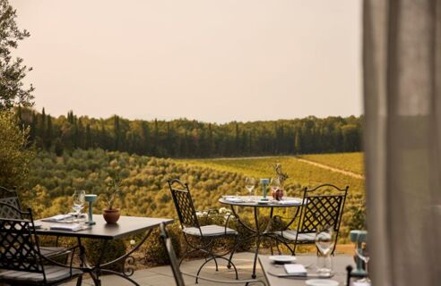 Outdoor dining tables with iron chairs set with glassware and napkins overlooking hills and vineyards at Podere San Filippo