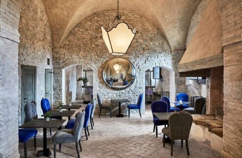 Dining area at Podere San Filippo featuring stone walls, arched ceilings, blue and gray upholstered chairs, and a large round mirror