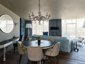 Living area with round dining table, upholstered chairs, blue sofa, and chandelier at COMO Alpina Dolomites hotel