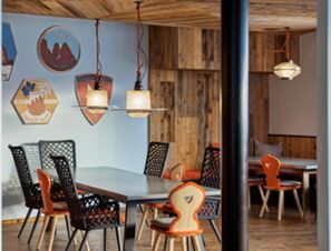 Dining area with wooden walls, mixed black and orange chairs, hanging lights, and COMO Alpina Dolomites decor signs