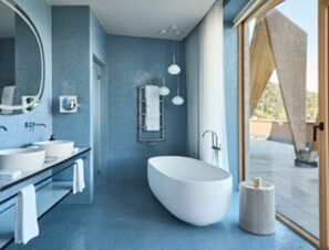 Modern bathroom at COMO Alpina Dolomites with a freestanding white bathtub, blue tiled walls, and large glass doors opening outside