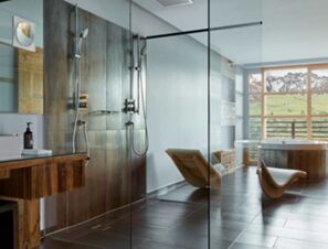 Modern bathroom with glass shower, wooden vanity, curved chairs, and mountain view at COMO Alpina Dolomites