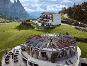 COMO Alpina Dolomites hotel with circular architectural structure, outdoor seating, and mountain scenery in background
