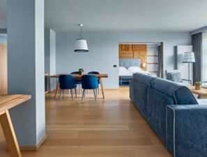 Living area with blue sofa and dining table with chairs near bedroom room in COMO Alpina Dolomites hotel