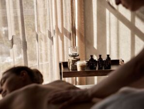 A person receiving a back massage near a wooden tray with oil bottles and a candle at COMO Alpina Dolomites spa room