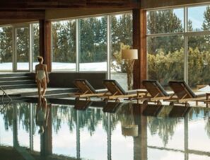 An indoor pool area with wooden lounge chairs and large windows showing trees at COMO Alpina Dolomites