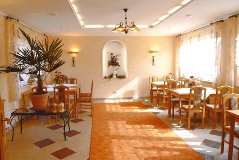 Dining area with wooden chairs and tables, decorated with plants and flowers at Privatpension Flemminger Hof