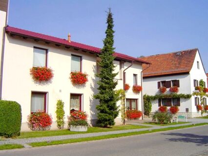 Die Au&szlig;enansicht der Privatpension Flemminger Hof zeigt wei&szlig;e H&auml;user mit roten Dachziegeln und blumengeschm&uuml;ckten Fenstern bei sonnigem Wetter.