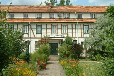 Die gepflegte Fassade des Sandgut Mihla Gasthof und Hotel mit traditionellem Fachwerk und einem blumengeschm&uuml;ckten Weg zum Eingang.