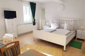 Helles und gem&uuml;tliches Schlafzimmer mit Doppelbett, Fernseher und gr&uuml;nen Vorh&auml;ngen im Sandgut Mihla Gasthof und Hotel.