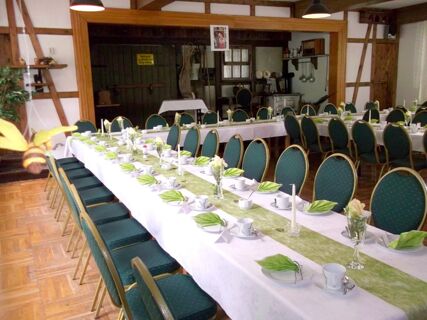 Gedeckte Tische mit gr&uuml;nen Servietten und wei&szlig;en Schalen in einem rustikalen Raum des Sandgut Mihla Gasthof und Hotel, Vorbereitung f&uuml;r ein Essen.