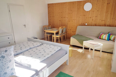 Helles Zimmer im Sandgut Mihla Gasthof und Hotel mit gem&uuml;tlichem Doppelbett, Esstisch und Couch vor Holzpaneelwand.