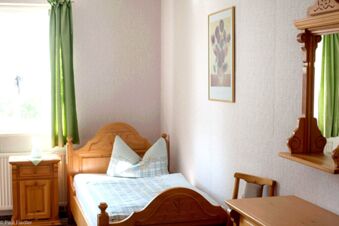 Hell eingerichtetes Einzelzimmer mit Holzm&ouml;beln, gr&uuml;nem Vorhang und schlichtem Wandbild im Sandgut Mihla Gasthof und Hotel.