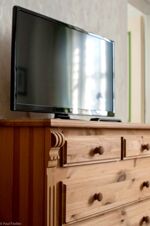 Moderner Flachbildfernseher steht auf einem h&ouml;lzernen Kommodenschrank in einem Zimmer des Sandgut Mihla Gasthof und Hotels.