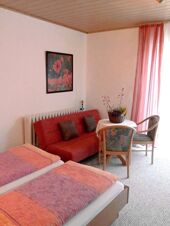 Hotel Zu den Schildb&uuml;rgern room with two single beds, a red sofa, two chairs around a table with a plant, and pink curtains