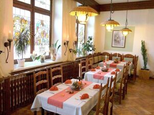 Dining area at Hotel Zu den Schildb&uuml;rgern with wooden chairs, white tables, orange napkins, hanging lamps, and stained glass windows
