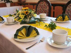 Table set with white cups, green and yellow folded napkins, floral centerpiece, and chairs at Hotel Zu den Schildb&uuml;rgern