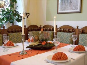 Dining table set with orange napkins, glassware, two lit candles, and a floral centerpiece at Hotel Zu den Schildb&uuml;rgern