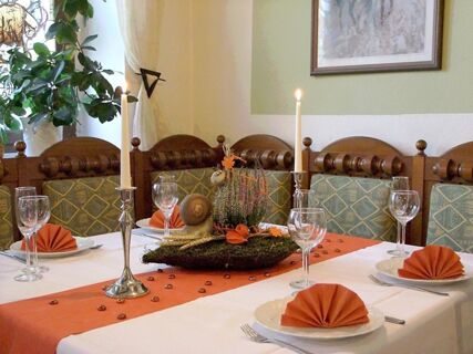 Dining table set with orange napkins, glassware, two lit candles, and a floral centerpiece at Hotel Zu den Schildb&uuml;rgern