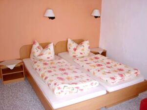 Two single beds with floral patterned bedding in a simple room at Hotel Zu den Schildb&uuml;rgern with wall lamps and nightstands