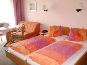 Hotel Zu den Schildb&uuml;rgern bedroom with twin beds featuring orange and pink bedding, a small seating area, and a window with curtains