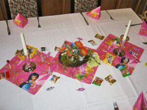 A white tablecloth-covered table at Hotel Zu den Schildb&uuml;rgern decorated with pink princess-themed napkins, candy, candles, and a floral centerpiece