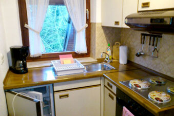 Kitchen area at Pension Haus Wiehenperle with wooden countertops, a sink, coffee maker, stove, and window with white curtains