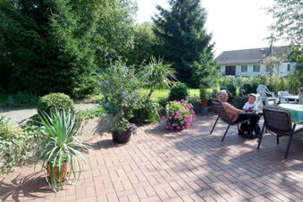 Two people sitting near a table with chairs on a brick patio surrounded by potted plants at Pension Haus Wiehenperle