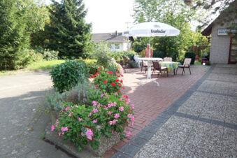 Outdoor seating area with tables, chairs, an umbrella, and flower beds at Pension Haus Wiehenperle garden patio