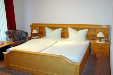 Double wooden bed with white linens and pillows in a room at Pension Haus Wiehenperle with armchair and bedside lamps