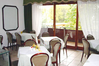 Dining area with tables covered in white tablecloths and chairs near large windows and balcony at Pension Haus Wiehenperle