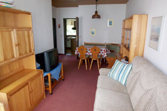 Living room with beige sofa, wooden furniture, TV on a small table, and a dining area at Pension Haus Wiehenperle