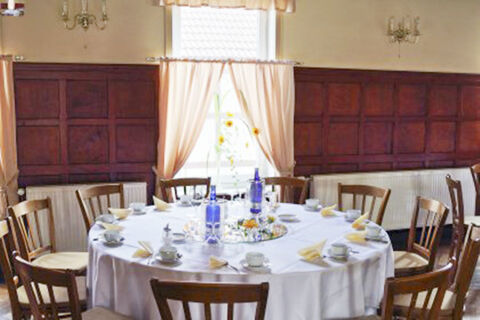 Round dining table with white tablecloth set with cups, blue bottles, and folded napkins in Hotel Restaurant Illemann dining room