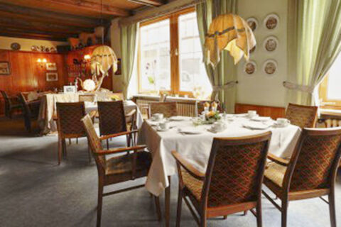 Dining area in Hotel Restaurant Illemann with tables covered in white cloths, vintage lamps, and wooden chairs arranged around them