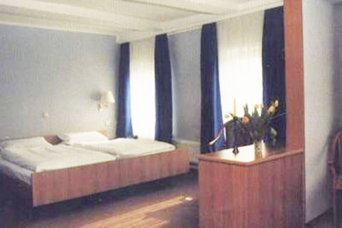 A hotel room at Hotel Restaurant Illemann with two beds, blue and white curtains, a flower vase on a wooden cabinet, and light gray walls