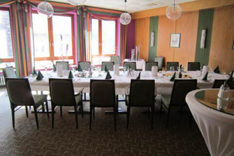 Dining area with a large U-shaped table set with white linens and green napkins in Hotel Restaurant Illemann