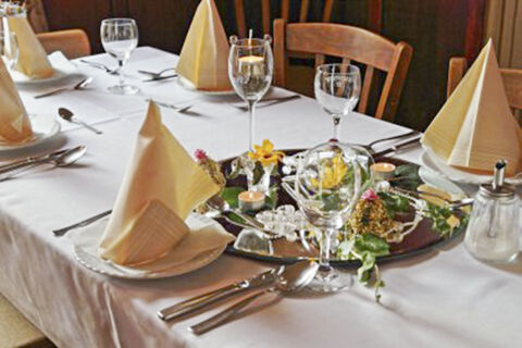 Table set with folded napkins, wine glasses, cutlery, and floral decorations at Hotel Restaurant Illemann