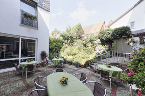 Outdoor patio seating area with metal chairs and tables covered in green cloths at Hotel Restaurant Illemann surrounded by plants