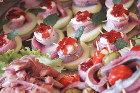Close-up of various appetizers with sliced meat, cheese, red berries, and herbs arranged on lettuce at Hotel Restaurant Illemann