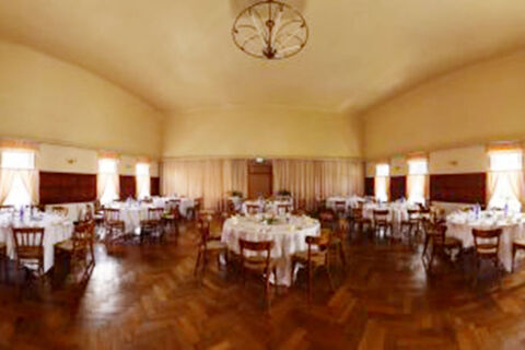 Round tables with white tablecloths and wooden chairs are set up in a large dining room at Hotel Restaurant Illemann