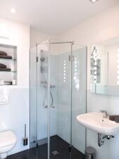Helles und modernes Badezimmer mit Glasdusche, Waschbecken und Toilette im JU 52 Hotel Arnsberg, ausgestattet mit Handt&uuml;chern und Hygienemitteln.