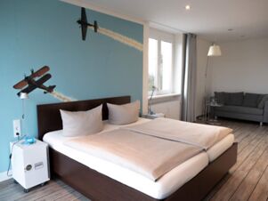 Modern eingerichtetes Zimmer mit gro&szlig;em Doppelbett, Sofa und Luftfahrt-Wanddekoration im JU 52 Hotel Arnsberg.
