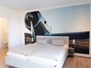 Modernes Hotelzimmer mit Doppelbett und gro&szlig;er Wandgestaltung eines Flugzeugs im JU 52 Hotel Arnsberg, hell und einladend eingerichtet.