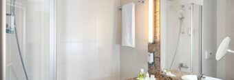 Bathroom interior at NH Hotel M&uuml;nchen Dornach with a shower, towel, mirror, sink, and toiletries on the countertop