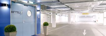 Blue door with a round window and the word HOTEL next to two potted plants in an underground parking at NH Hotel M&uuml;nchen Dornach