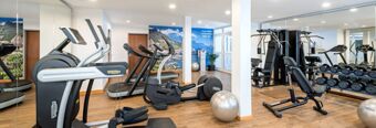 A spacious gym at NH Hotel M&uuml;nchen Dornach with treadmills, exercise bikes, weight machines, dumbbells, and stability balls