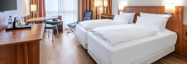 Two single beds with white linens, wooden headboard, desk with chair, and window with curtains in NH Hotel M&uuml;nchen Dornach room