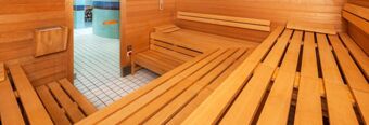 Interior view of a wooden sauna room with bench seating and an open door leading to a tiled corridor at NH Hotel M&uuml;nchen Dornach