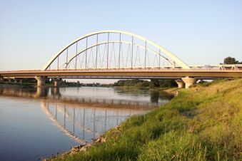 Peizažas su moderniu tiltu per ramią upę, apylinkėmis ir krantu prie pensiono "Zur Elbe" vakaro &scaron;viesoje.